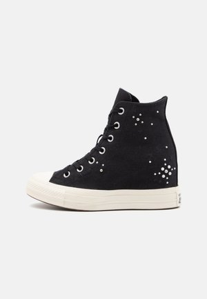 Black high-top sneaker with white sole and scattered pearl embellishments on canvas fabric, shown in profile against a neutral background.