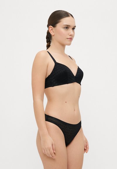 Conjunto de lencería negra que incluye un sujetador con relleno de escote pronunciado y un tanga a juego. La tela presenta un discretos patrón de logotipo. Las tirantes ajustables completan el diseño.