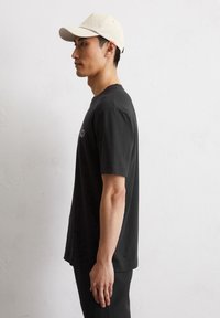 Zwart T-shirt met korte mouwen, ronde hals en een relaxed fit. Vergezeld door een lichtbeige pet met een gebogen rand en minimale details.