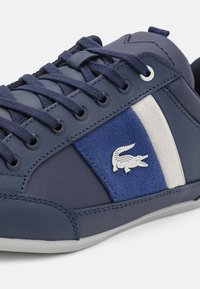 Baskets bleu marine avec lacets assortis, semelle blanche, panneau en daim et logo crocodile argenté sur le côté.