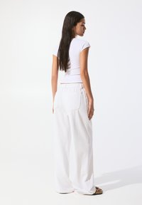 White, relaxed-fit linen trousers with a drawstring waist and two back pockets, paired with a fitted white short-sleeve shirt.