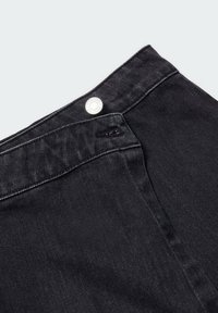 Pantalones de denim negro con una textura suave, que presentan un botón plateado en la cintura y sutiles detalles de costura a lo largo de los bordes.