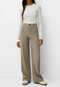 béžové kalhoty s širokým nohavicí a texturovaným vzorem, vysokým pasem a jednom knoflíku. V kombinaci s příjemným světle šedým topem s dlouhým rukávem.