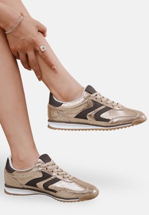 Baskets de sport dorées et noires avec une texture métallique, bout rond, design à laçage, et une semelle intermédiaire blanche avec une semelle extérieure en caoutchouc texturé.