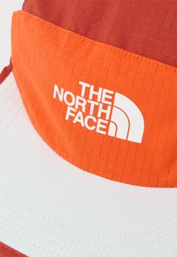 Πορτοκαλί και λευκό καπέλο με το λογότυπο The North Face τυπωμένο σε λευκό στην μπροστινή πορτοκαλί επιφάνεια.