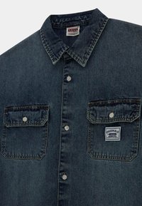 Denim overhemd in een donkere wassing met een klassieke kraag, twee borstzakken, zilveren knopen en een merketiket op de linkse zak.