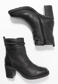 Botas de tobillo de cuero negro con tacón cuadrado, cremallera lateral y textura grabada en el tacón. Diseño suave y ligeramente caído.