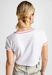 Camiseta blanca recortada con ribete rojo en el escote y las mangas. Textura suave, diseño clásico de cuello redondo y mangas cortas.