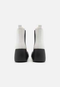Botas de tobillo blancas y negras de cuero suave, con una forma elegante, colores contrastantes, un tacón alto en cuña y pestañas en la parte trasera.