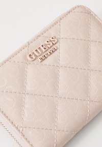 Light pink quilted wallet made of textured material, featuring embossed logo and stitching details. Zipper closure at the edge.