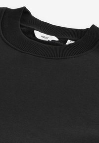 Svart sweatshirt med rund halsringning och ribbad detalj. Tillverkad av mjukt material, den har en slät yta och en synlig etikett vid halsen.