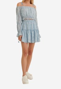 Off-the-shoulder, lyseblå blomsterkjole med lange ærmer, flæsekant og elastisk talje; parret med hvide sneakers.