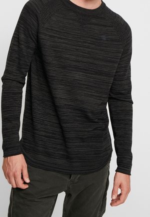 Zwart gestreept shirt met lange mouwen, gemaakt van zachte stof, met een ronde halslijn en een licht gebogen zoom. Minimale branding op de borst.