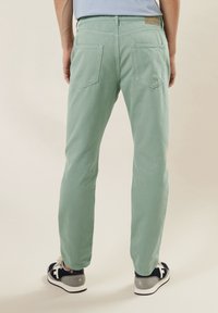 Lichtgroene katoenen broek met een rechte pijp, voorzien van twee achterzakken en een leren label op de tailleband. Draag met blauwe en grijze sneakers.