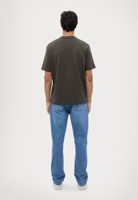 Camiseta de manga corta verde oscuro combinada con jeans de mezclilla azul claro, con corte recto y bolsillos traseros. Diseño simple, estilo casual.