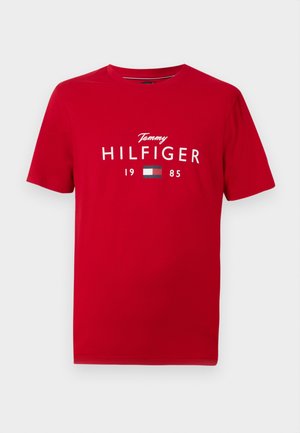 Rød kortærmet T-shirt med rund halsudskæring, der har teksten "Tommy Hilfiger 1985" i hvidt og mærkets flaglogo centreret på brystet.