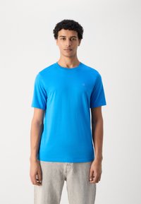 Svijetloplavi kratki rukav T-shirt od mekog materijala s okruglim izrezom, koji ima mali logo na lijevoj strani prsnog koša.