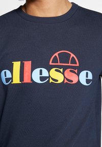 T-shirt in cotone blu navy con il logo "ellesse" in rosso, giallo, azzurro e blu scuro, accompagnato da un design semicircolare sopra il testo.