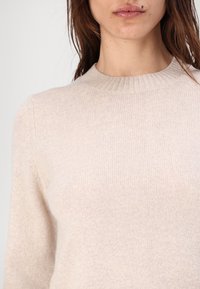 Jasno-beżowy sweter z ribbowym splotem, okrągłym dekoltem i długimi rękawami, charakteryzujący się miękką fakturą oraz dopasowanym krojem.