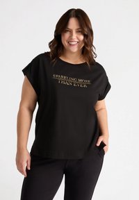 Schwarzes Baumwoll-T-Shirt mit kurzen, aufgerollten Ärmeln und einem runden Ausschnitt. Vorn bedruckt mit goldenem Text "SPARKLING MORE THAN EVER".