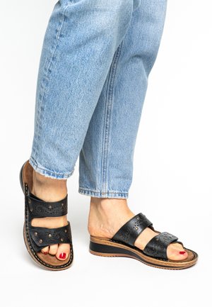 Black leather sandals with two wide straps featuring cut-out patterns and metal accents. Comfortable flat sole with a textured base.