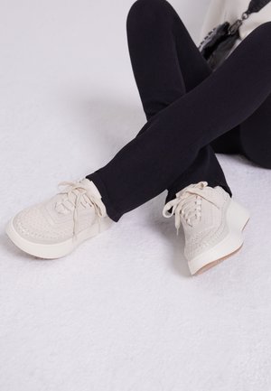 Weiße Sneakers mit strukturiertem, gewebtem Design und erhöhter Sohle, mit Schnürverschluss und subtilen Details entlang der Kanten.
