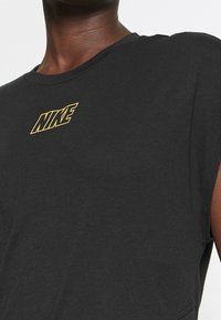 Camiseta de algodón negra con cuello redondo y mangas cortas. Presenta un logo de Nike amarillo centrado en el pecho, con una textura que parece suave.