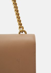 Tan leather handbag featuring a smooth texture, rounded shape, and a large gold chain strap with a branded metal accent.