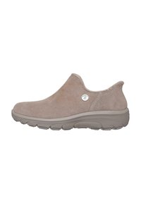 Zapato slip-on de ante beige con puntera redondeada, parte superior texturizada y suela de goma flexible. Presenta un acento metálico con el logo en el lateral.
