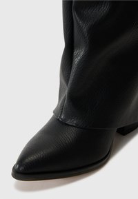 Botín de cuero negro hasta el tobillo con punta afilada, acabado texturizado y tacón bajo. Presenta un diseño gathered en el tobillo.
