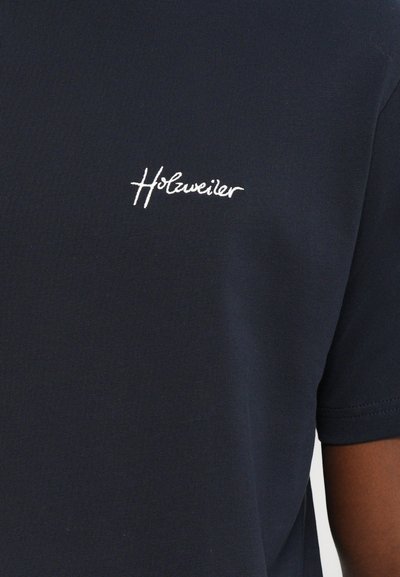 Tumši zilas kokvilnas T-krekls ar īsām piedurknēm, kuram uz kreisā krūšu ir balta izšūta logo "Holzweiler". Gluda tekstūra, klasiskā piegriezuma.