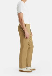 Pantalon kaki droit en mélange de coton, avec poches latérales et texture lisse. Porté avec un t-shirt blanc et des baskets blanches.