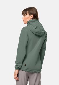 Veste à capuche résistante à l'eau en vert atténué. Caractéristiques : coupe décontractée, poignets élastiques et étiquette à l'ourlet. Texture lisse et élégante.