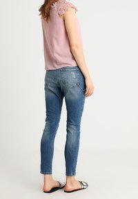 Blusa rosa con maniche in pizzo, abbinata a jeans skinny blu e sandali neri. L'outfit presenta una vestibilità comoda e denim lavato chiaro.