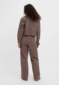 Brown-striped, cropped jacket with long sleeves paired with high-waisted, wide-leg pants. Features pockets and textured fabric.