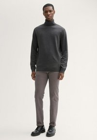 Donkergrijze coltrui met lange mouwen, gecombineerd met lichtgrijze broek en zwarte veterschoenen. Glad materiaal, smalle pasvorm.