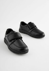 Chaussures en cuir noir avec une bande Velcro, bouts ronds, détails de couture et semelles en caoutchouc pour une meilleure traction. Design simple, silhouette basse.