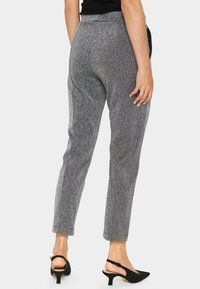 Szare, błyszczące spodnie taperowane z wysokim stanem i bocznymi kieszeniami, zestawione z czarnymi szpilkami na odkrytej pięcie. Gładka faktura i dopasowany krój.