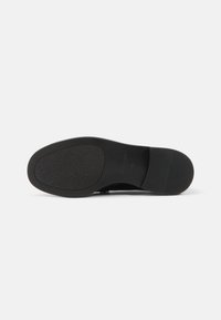 Schwarze Schuhsohle mit einem glatten, flachen Design. Strukturierte Gumm Oberfläche für besseren Grip, dezentes Branding nahe der Ferse und abgerundete Zehenform.
