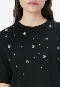 Zwarte katoenen t-shirt met ronde versieringen, waaronder parels en strass-steentjes, in een willekeurig patroon op de voorkant.