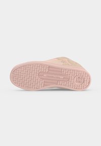 Semelle d'une basket rose clair avec motif d'adhérence texturé, texte « DCSHOECOUSA » et logo circulaire près du talon, présentée sur un fond uni.