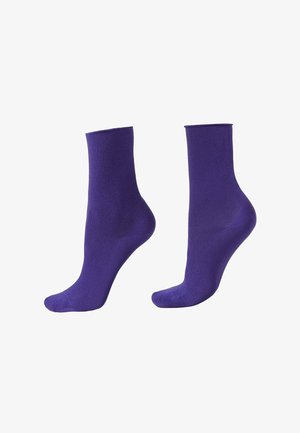 Par de calcetines lisos morados hasta el tobillo, mostrados sobre formas de pie invisibles contra un fondo blanco.