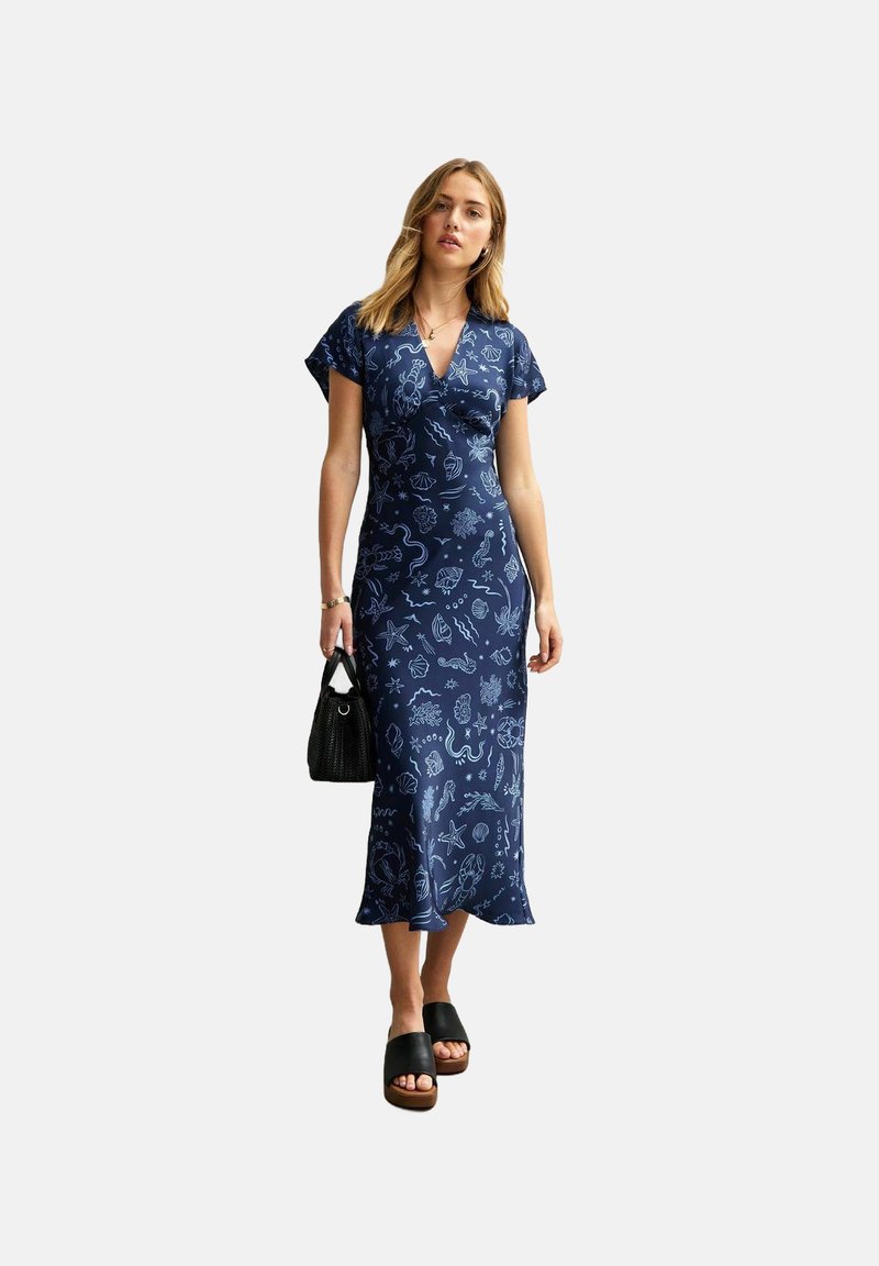 Robe bleu marine avec un décolleté en V et des manches courtes, ornée d'un motif léger inspiré de la mer en bleu clair. Texture lisse ; associée à des sandales à plateforme noires.