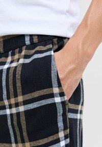 Pantaloni corti a scacchi neri e marroni con una texture in cotone, dotati di una tasca laterale e di una mano visibile che si trova all'interno.