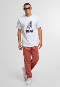 Weißes Grafik-T-Shirt mit dem Text "UNFAIR" und bunter Illustration, kombiniert mit rosa Jogginghosen und weißen Turnschuhen.