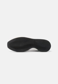 Hvit såle på sneakers med teksturert svart gummi yttersåle som har bølgemønstre for grep og trekkraft, designet for komfort og stabilitet.