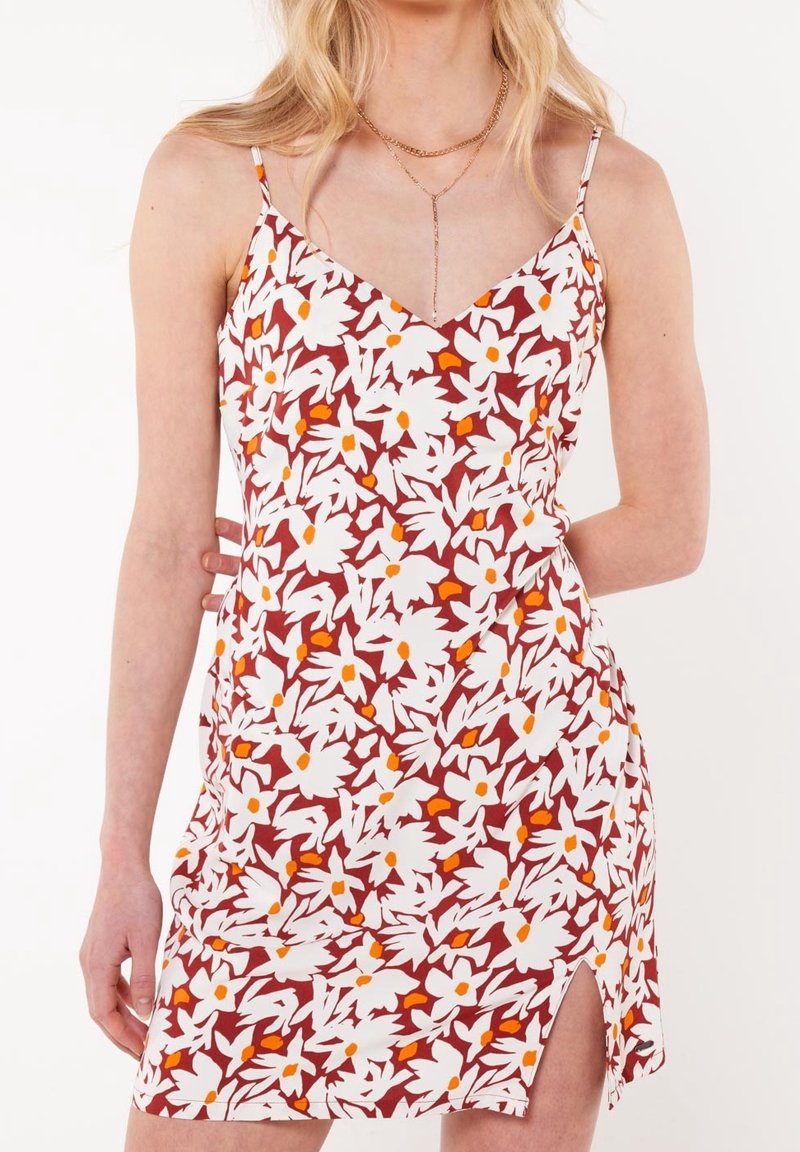 Woman wearing sleeveless floral dress with red, white, and orange pattern, featuring a side slit and thin shoulder straps, accessorized with gold necklaces.