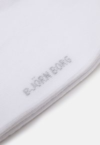 Weißer Baumwollsocken mit feiner Rippstruktur, ausgestattet mit einem kleinen grauen Logo, das nahe dem Bündchen gestickt ist. Flaches und gefaltetes Design.