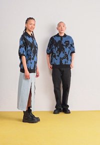 Δύο άτομα με υπερμεγέθεις πλεκτές μπλούζες μπλε και μαύρου σχεδίου. Το ένα συνδυάζεται με μια μακριά τζιν φούστα και το άλλο με μαύρες παντελόνες και μποτάκια.