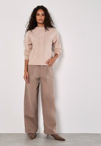 Jasnoróżowy sweter dzianinowy z teksturowanym wzorem w chevron, zestawiony z beżowymi spodniami o szerokich nogawkach oraz taupe szpilkami.